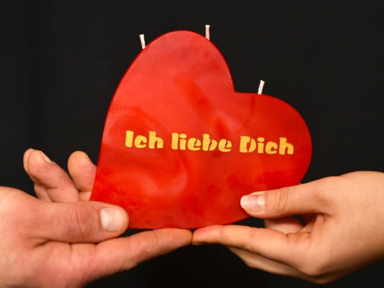 Rote Herzkerze mit der Aufschrift "Ich liebe Dich" in Händen gehalten