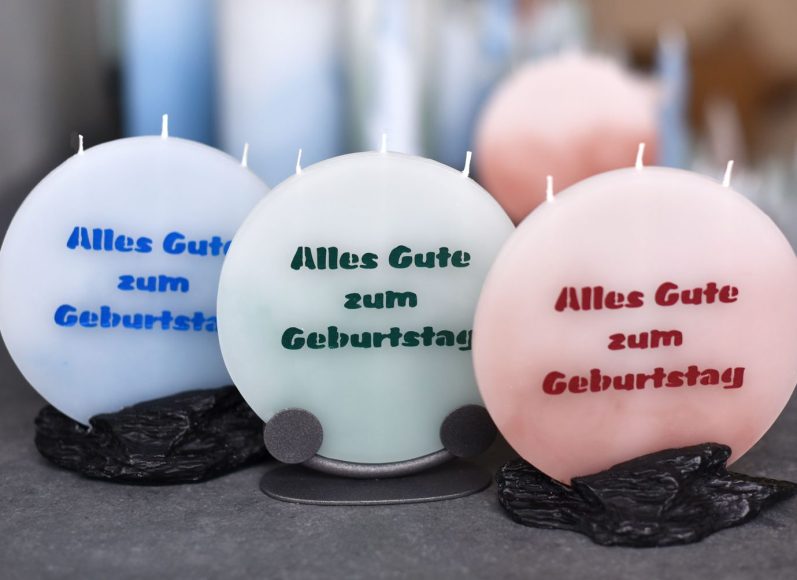 Drei runde Kerzen mit der Aufschrift 'Alles Gute zum Geburtstag' in Blau, Grün und Rot