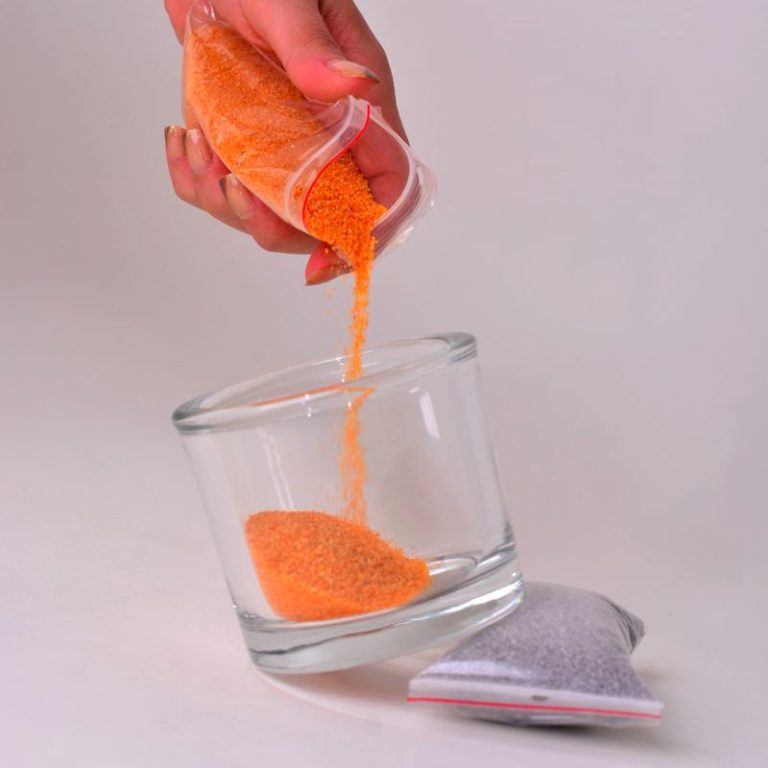 Person gibt orangefarbenen Sand in ein Glas